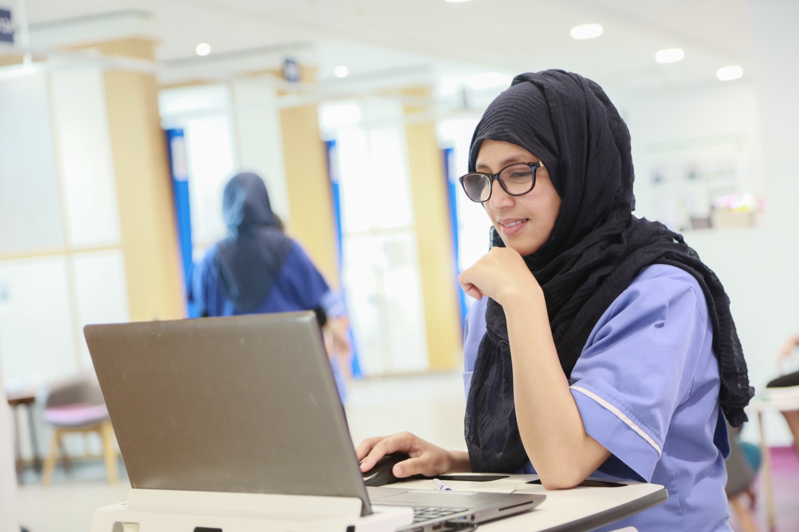 Female nurse in hijab on CCC-Liverpool chemotherapy unit. She is working at a computer and smiling