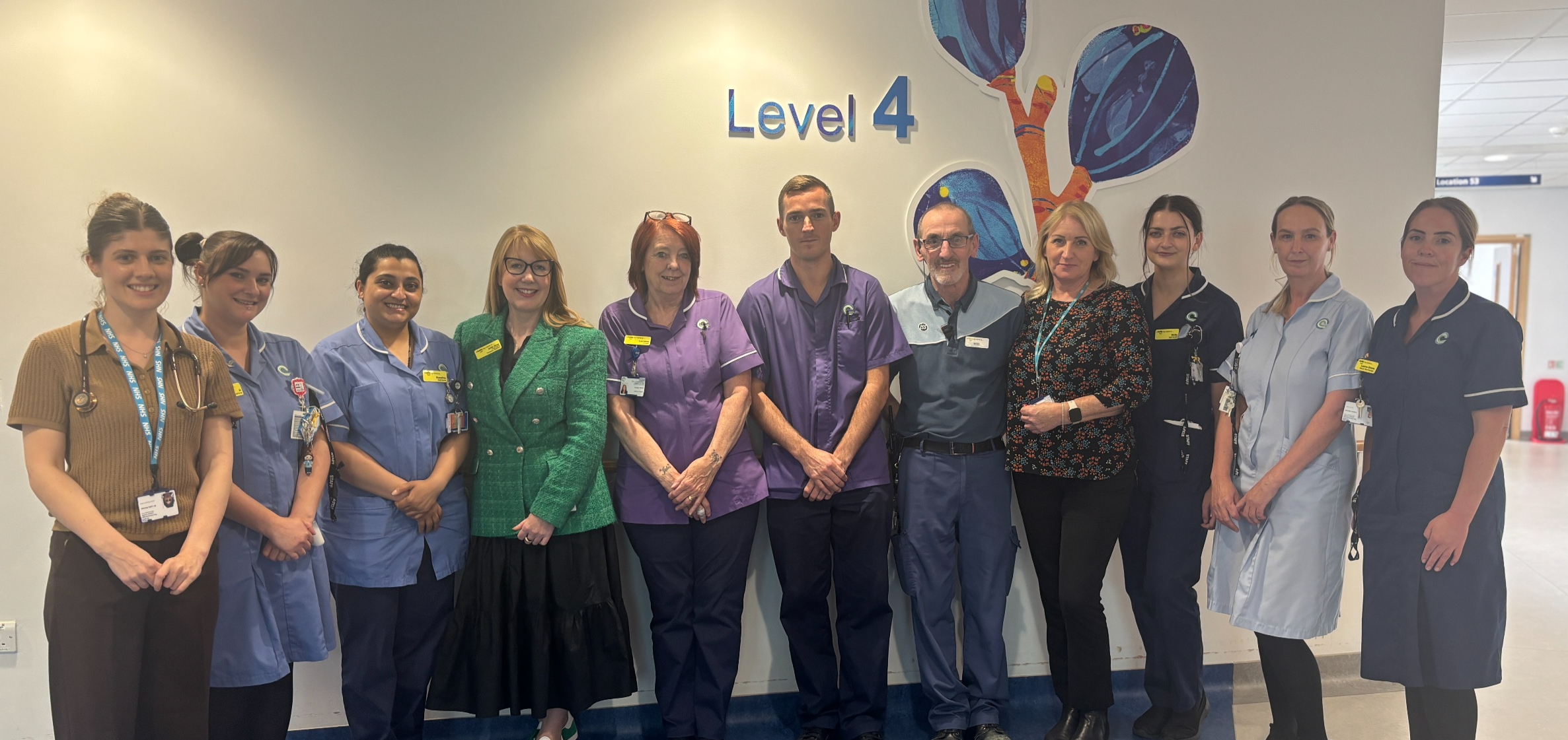 A group of staff in nurses and other uniform stand outside a sign that says Level 4 