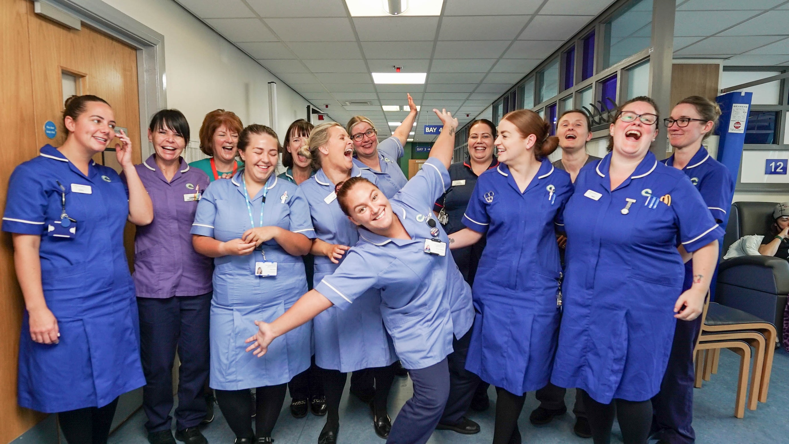 Group shot of the Delamere chemotherapy unit nursing team. They are waving their arms in the air and laughing
