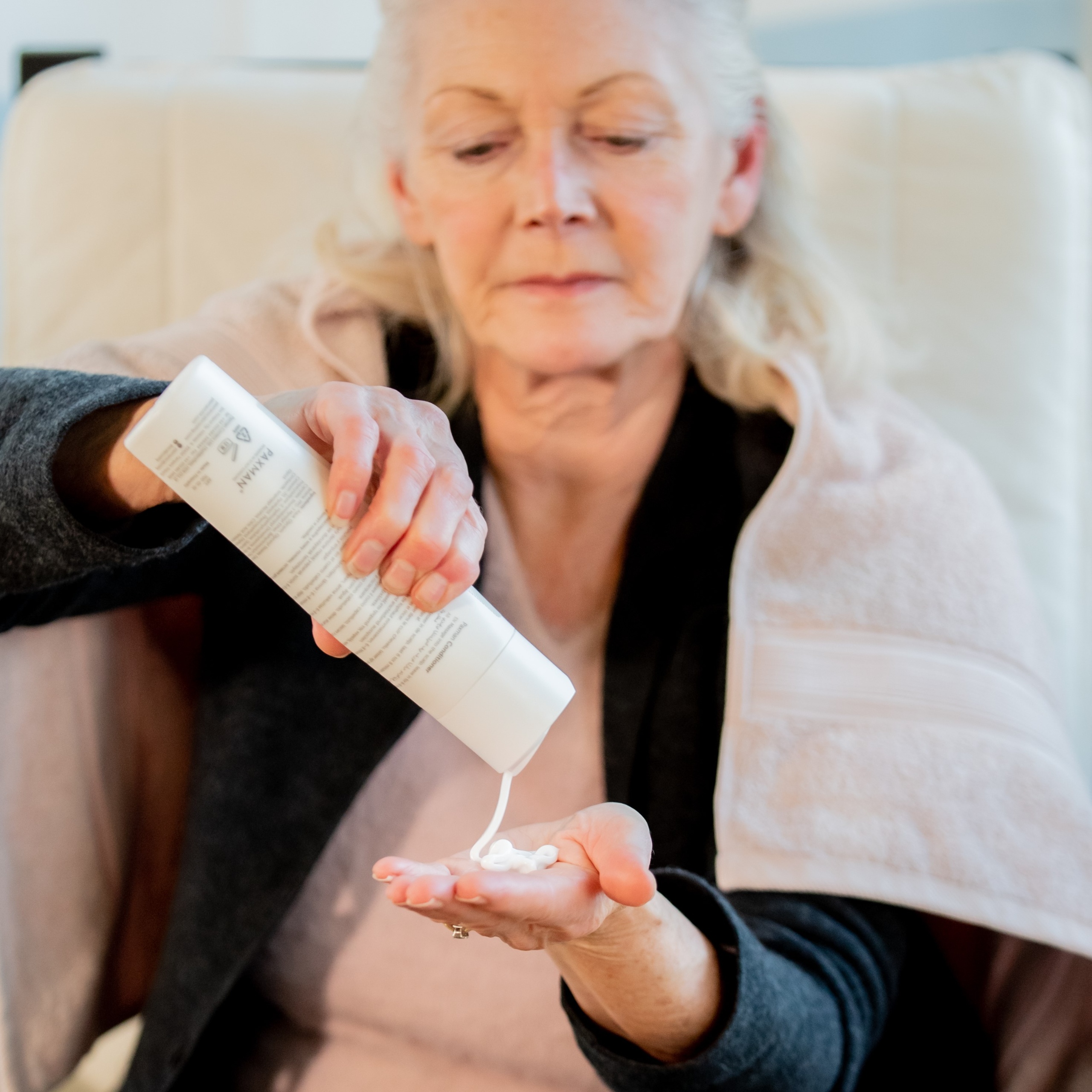A woman is pouring hair conditioner into her hand to put on her hair before using the scalp cooling machine