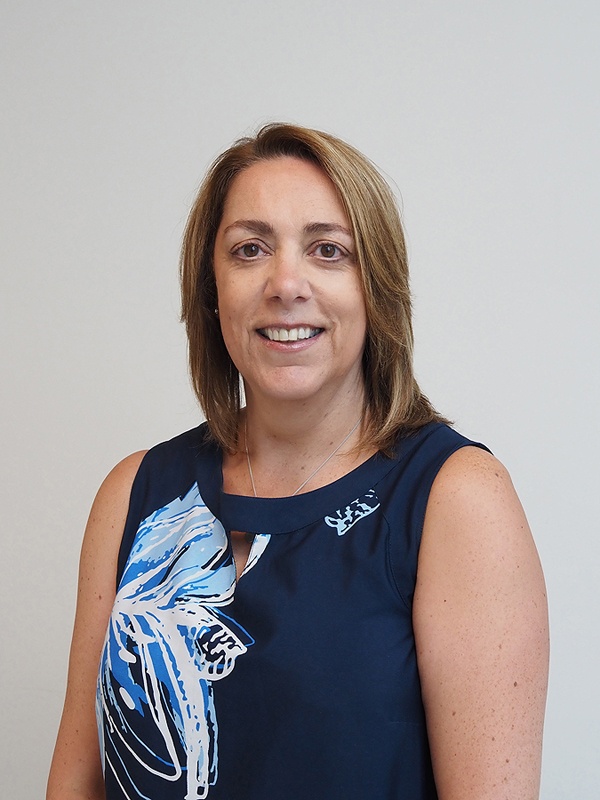 Jo has dark hair and eyes. She is smiling and wears a navy sleeveless dress